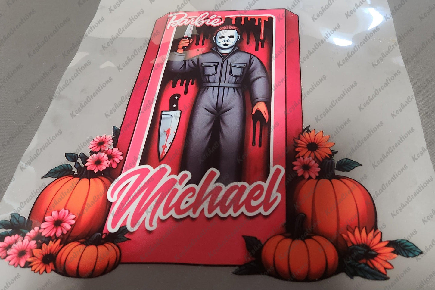 DTF transfer design featuring Michael Myers inside a pink Barbie box, with a blood-stained knife and surrounded by pumpkins and flowers, with 'Michael' written at the bottom.