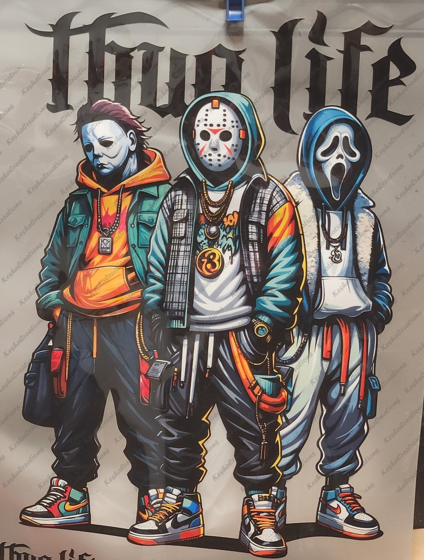 DTF transfer design featuring Michael Myers, Jason Voorhees, and Ghostface dressed in colorful, urban-inspired outfits, complete with hoodies, chains, and sneakers, under Gothic 'Thug Life' lettering. The trio stands confidently, showcasing their street-style personas.
