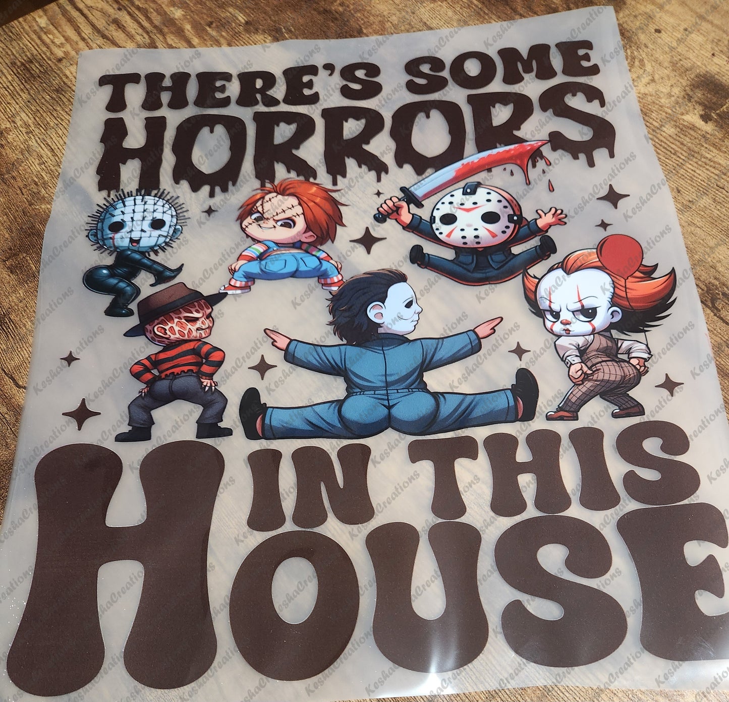 DTF transfer sheet showing Pinhead, Chucky, Jason Voorhees, Michael Myers, and Pennywise in a twerking pose under 'There's Some Horrors in This House' text in dripping letters.