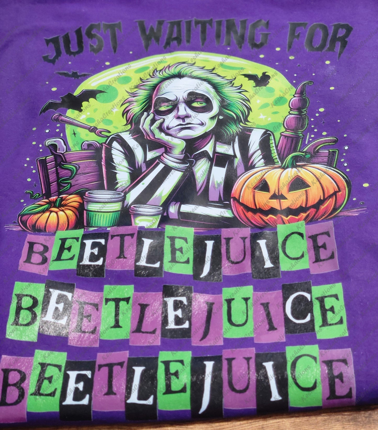 Purple T-shirt design featuring Beetlejuice sitting with a bored expression, surrounded by Halloween elements like pumpkins, bats, and spooky details, with the phrase 'Just Waiting for Beetlejuice' above in eerie lettering.